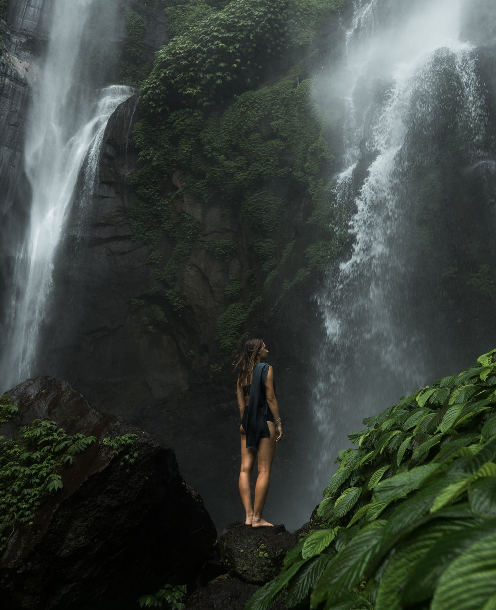 Woman with Nanodry towel standing in front of lush green waterfall