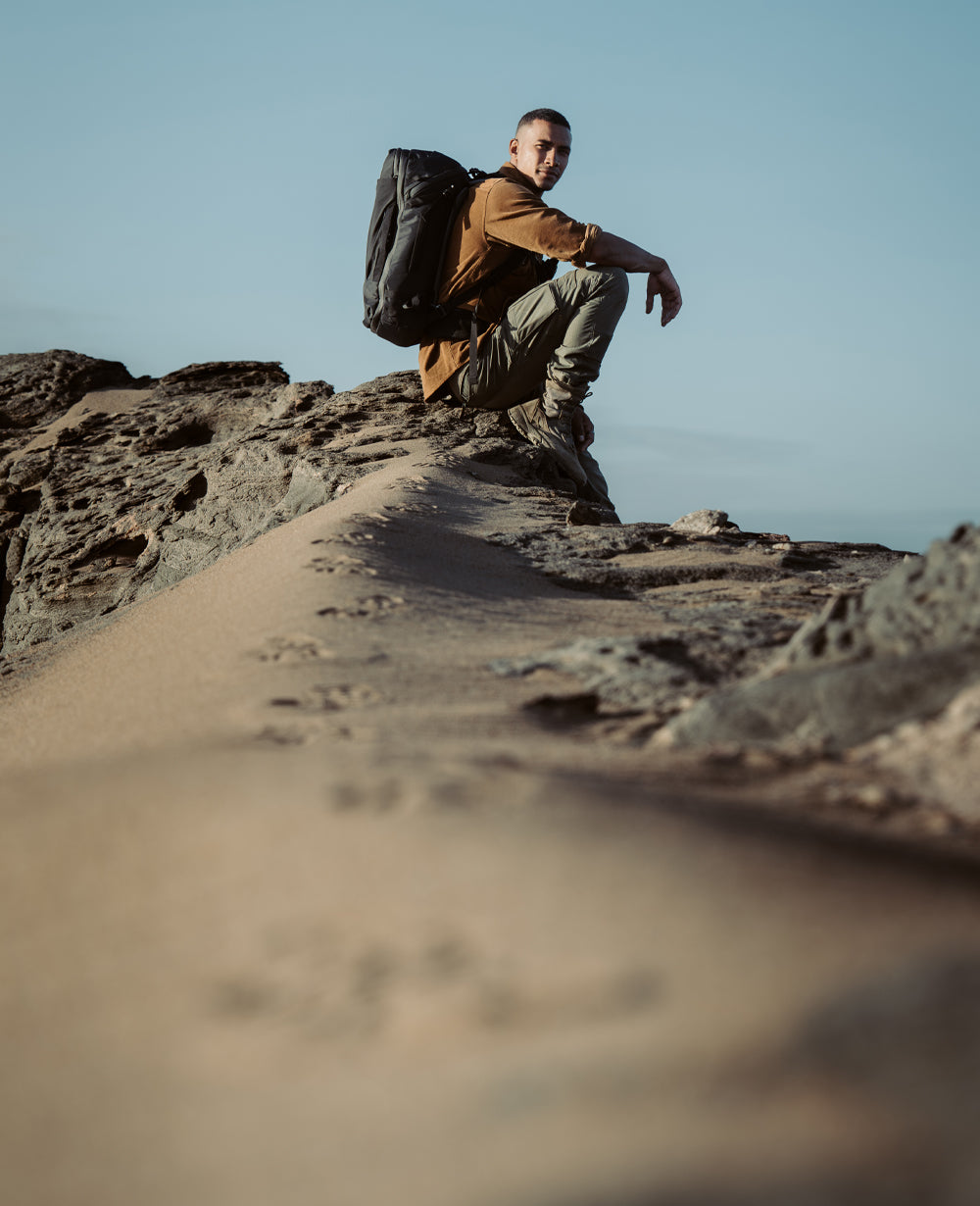 Man sitting in rocky desert setting, wearing black GlobeRider35 Travel Pack