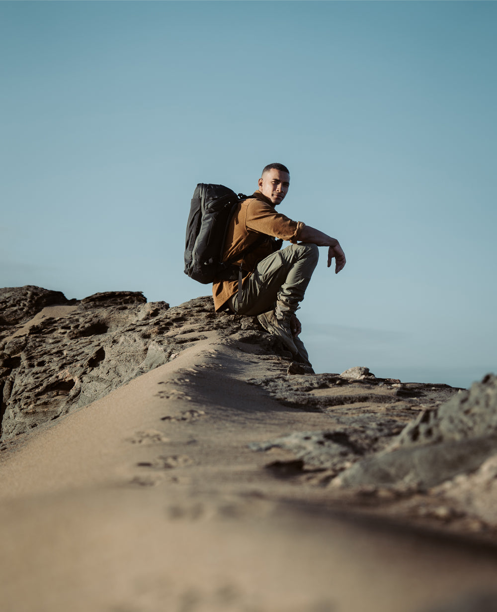Man sitting in rocky desert setting, wearing black GlobeRider35 Travel Pack