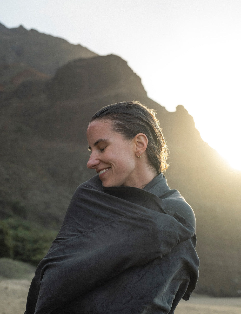Woman on sunset beach, wrapping herself in a nanodry towel