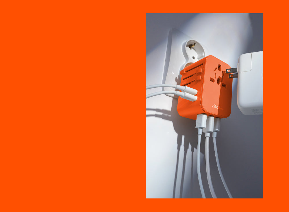 Bright orange background with image overlaid of orange travel adapter plugged into outlet, full of cords 