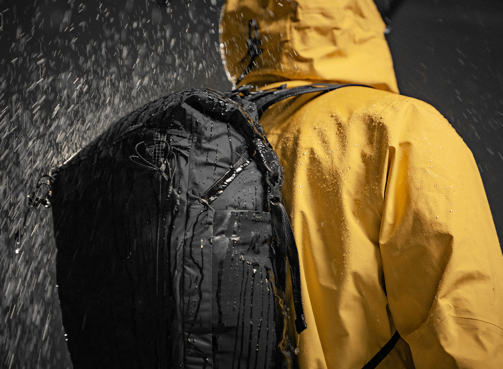 person wearing yellow jacket and black backpack being soaked by rain