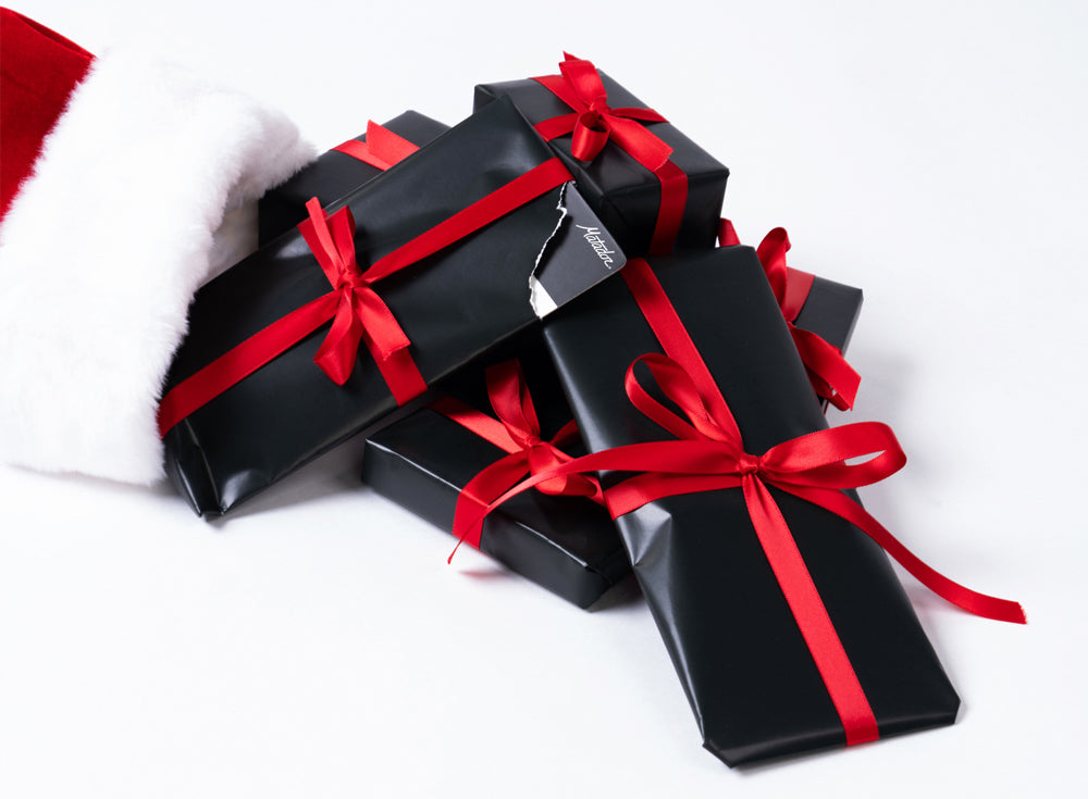 black wrapped gifts with red ribbon coming out of stocking on white background