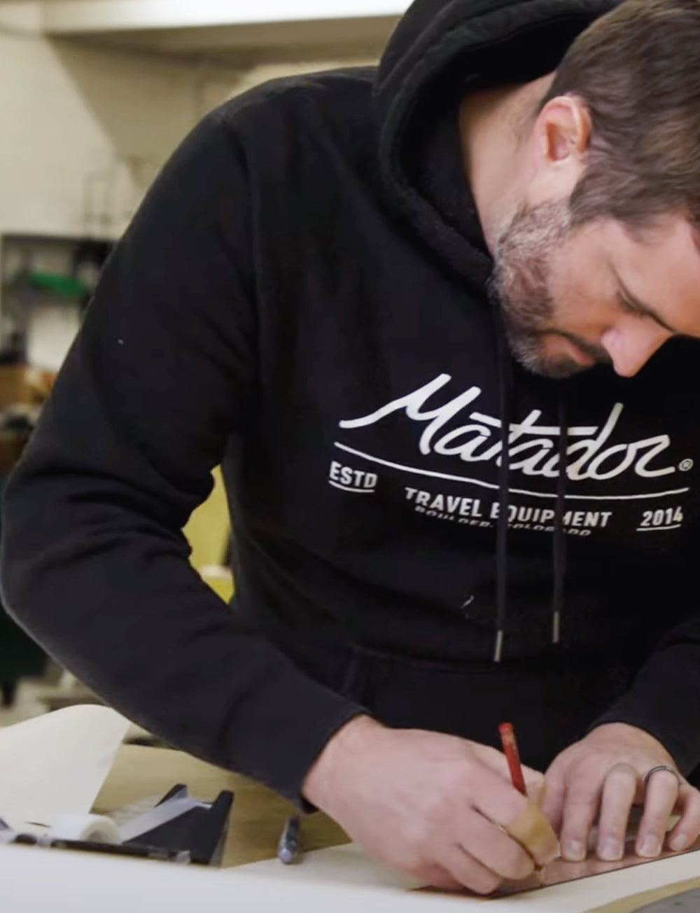 Man wearing black matador sweatshirt drawing at a work table