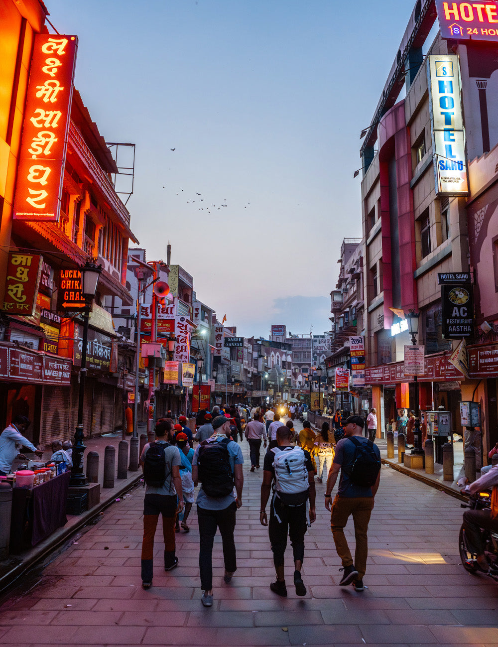 4 men walking down Indian street lit up by neon lights