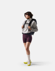 Person wearing a gray jacket, maroon shorts, and yellow shoes with a black backpack on a white background