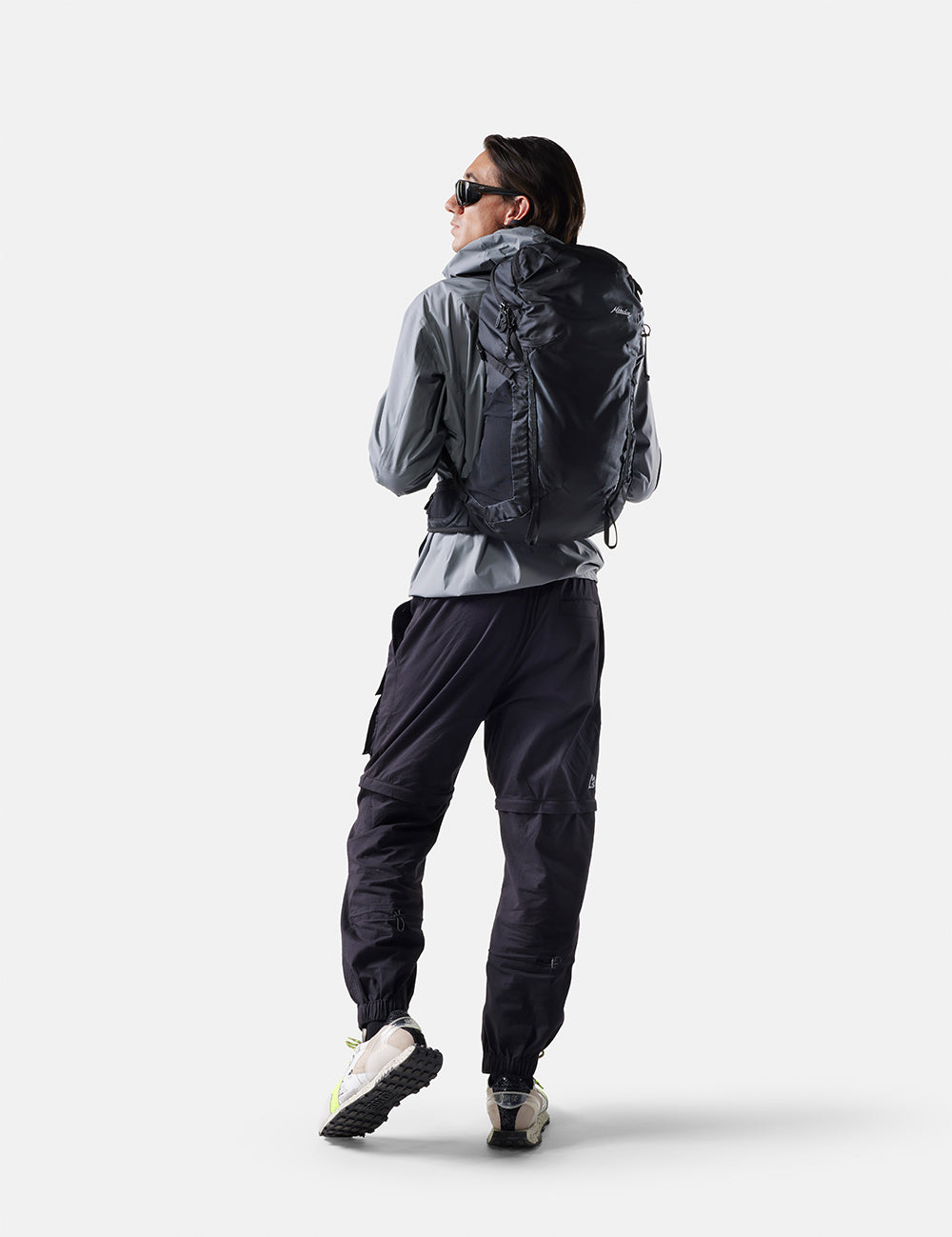 Person wearing a gray jacket and black pants with a backpack on a white background