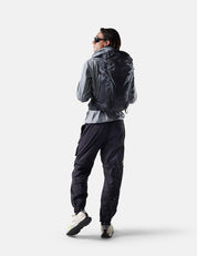 Person wearing a gray jacket and black pants with a backpack on a white background