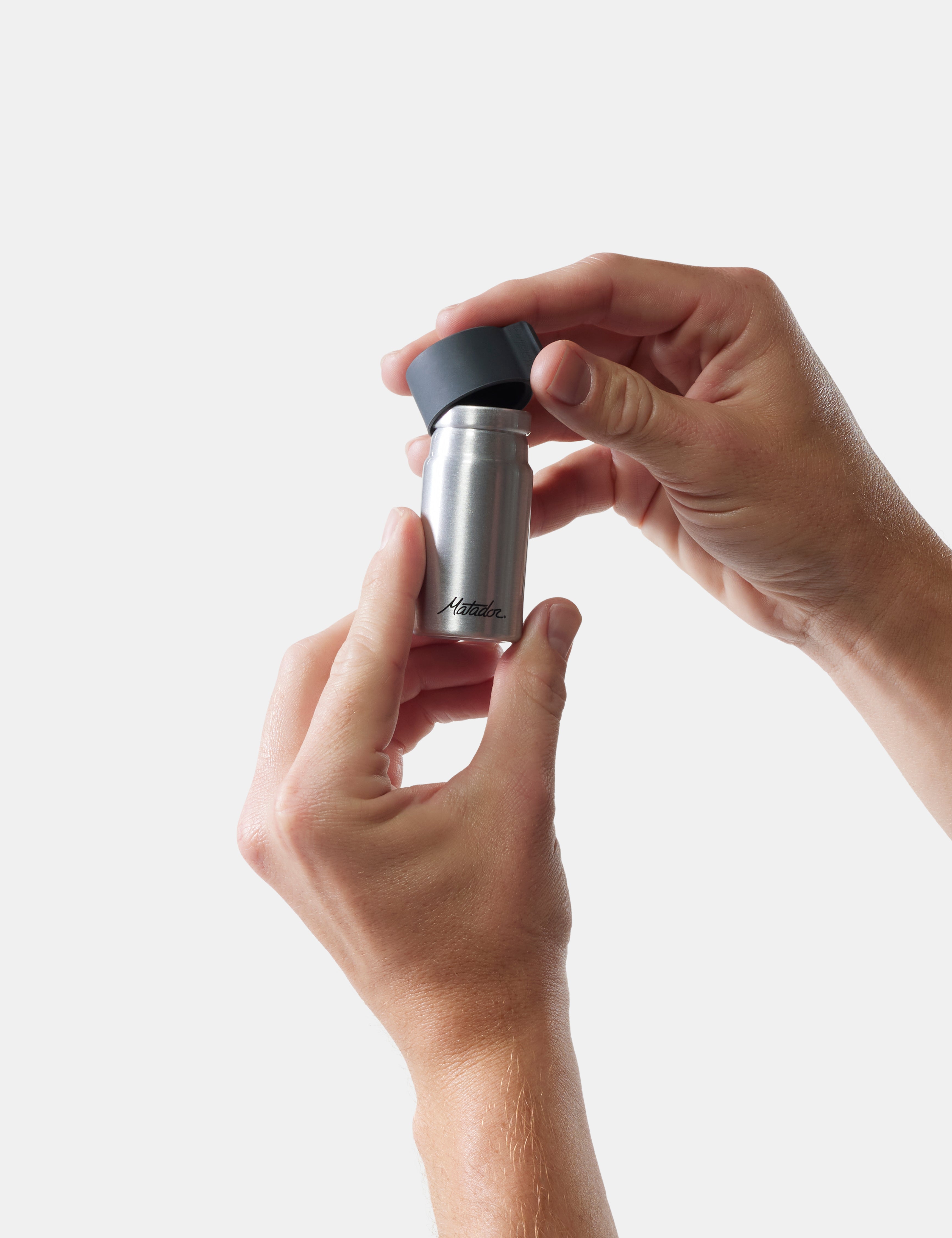 Person holding a silver and black container against a white background
