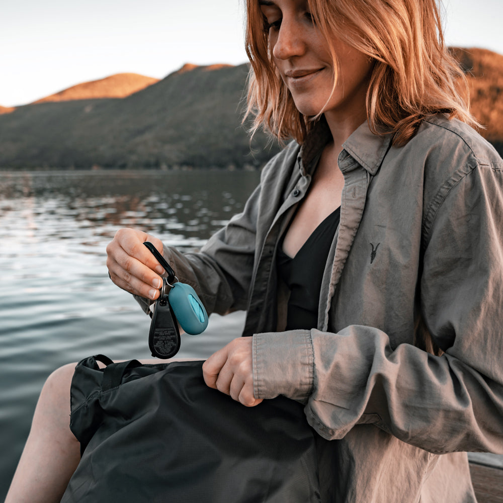 Woman at alpine lake, taking blue droplet case out of her bag