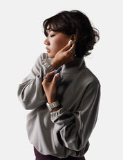 Woman wearing a light gray turtleneck sweater against a white background, putting in earplug