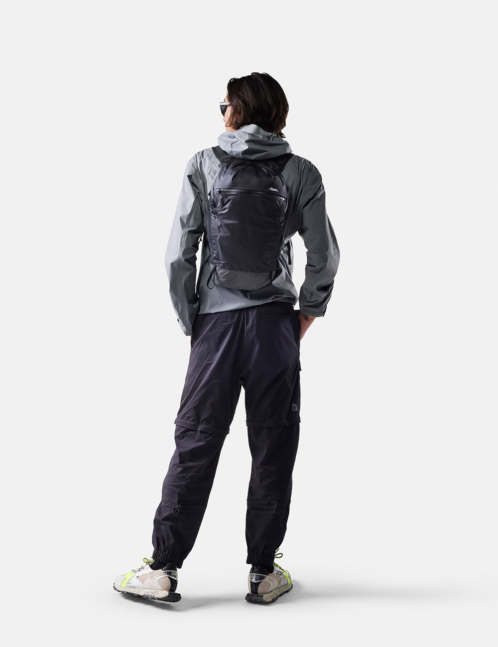Person wearing a gray and black raincoat with a backpack on a white background