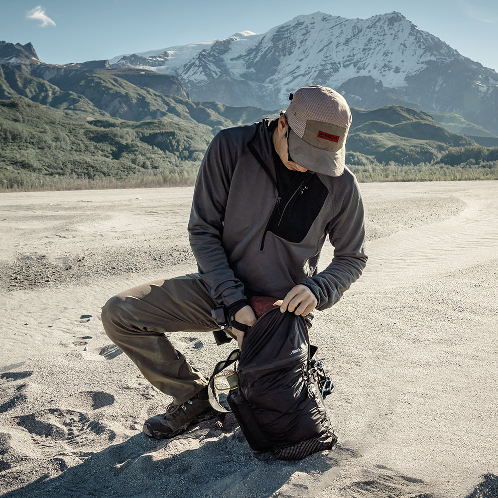 man kneeling on alaskan beach, reaching into black backpack