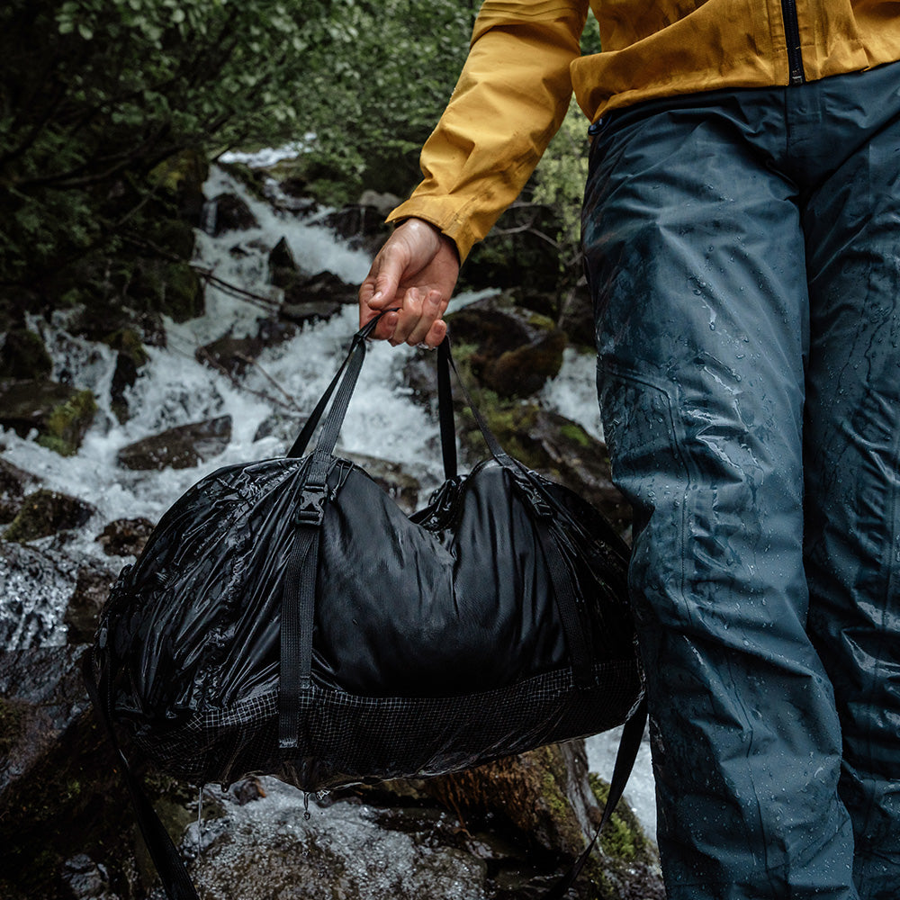 man soaking wet next to a waterfall, carrying black duffle
