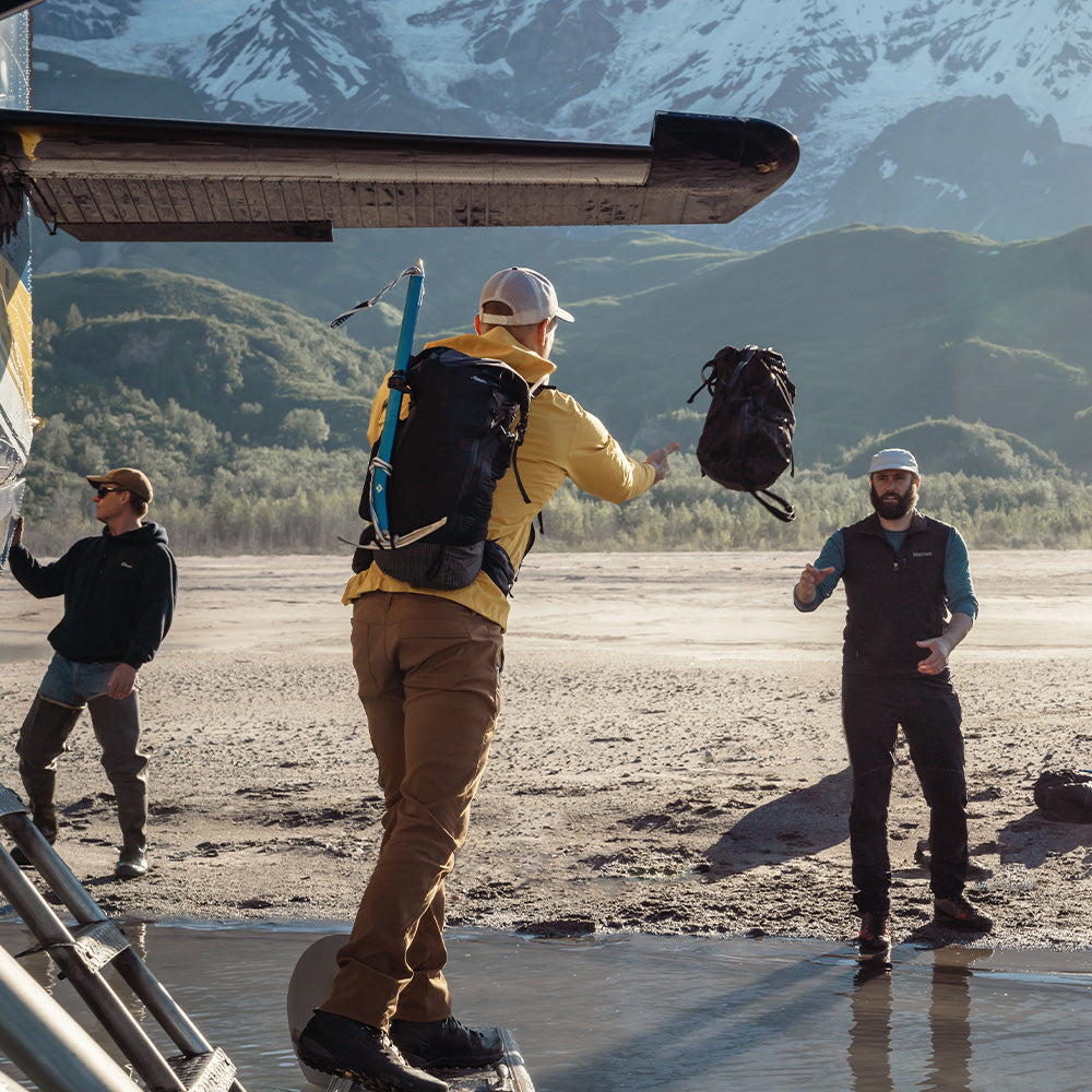 man tossing black duffle from sea plane to sandy shore