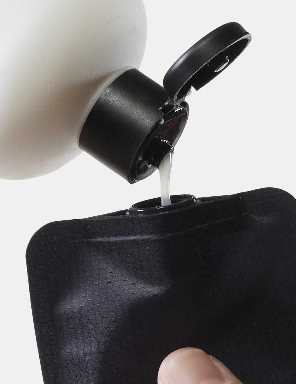 white bottle of liquid squeezing into mouth of black bottle