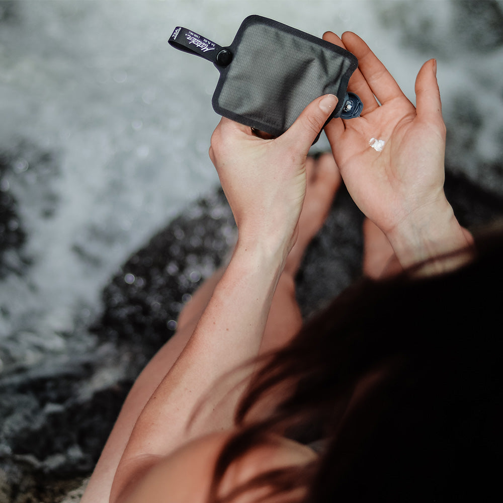 woman at waterfall, squeezing sunscreen into her hand from toiletry bottle