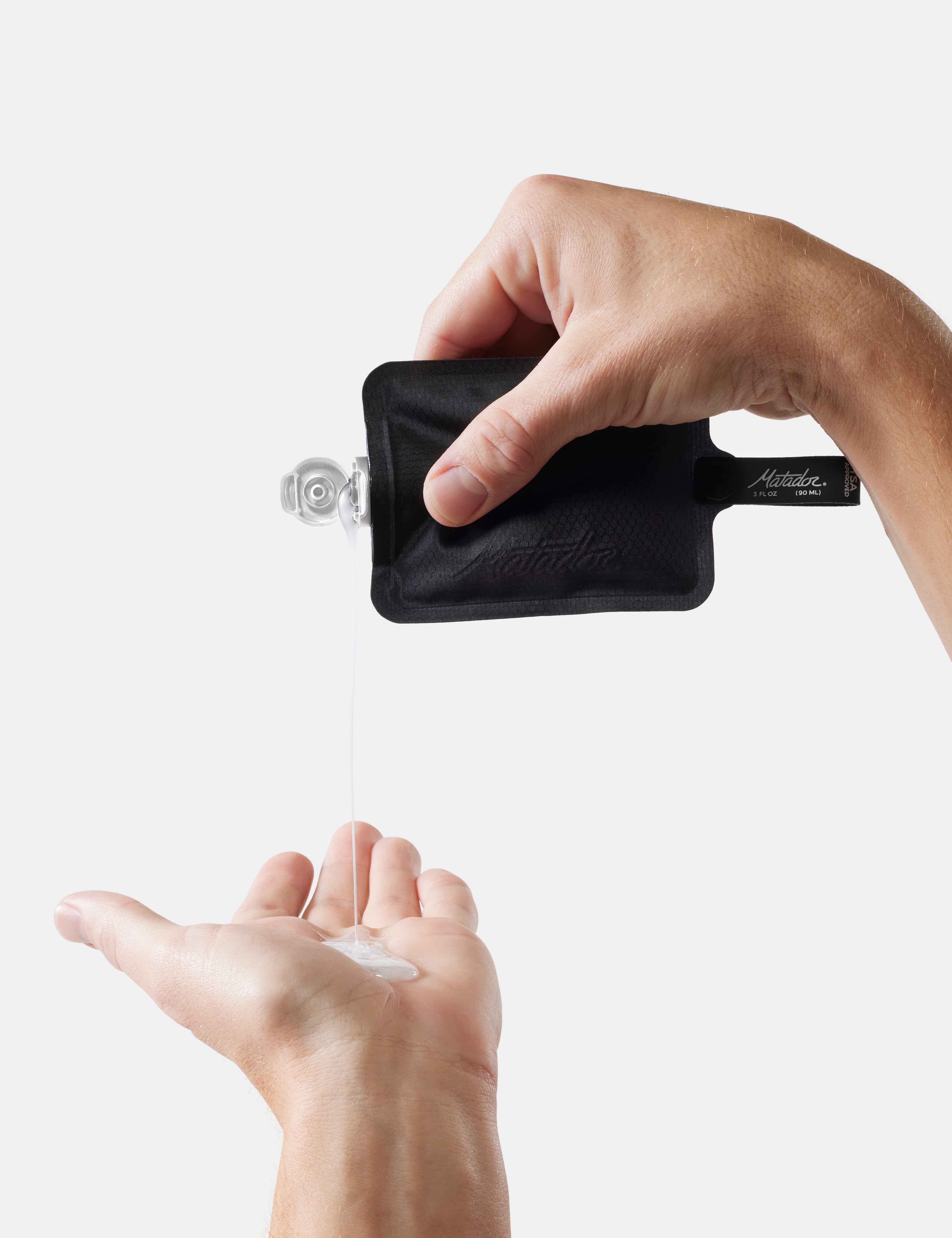 Hand using a black travel-sized bottle to dispense liquid soap into another hand on a white background