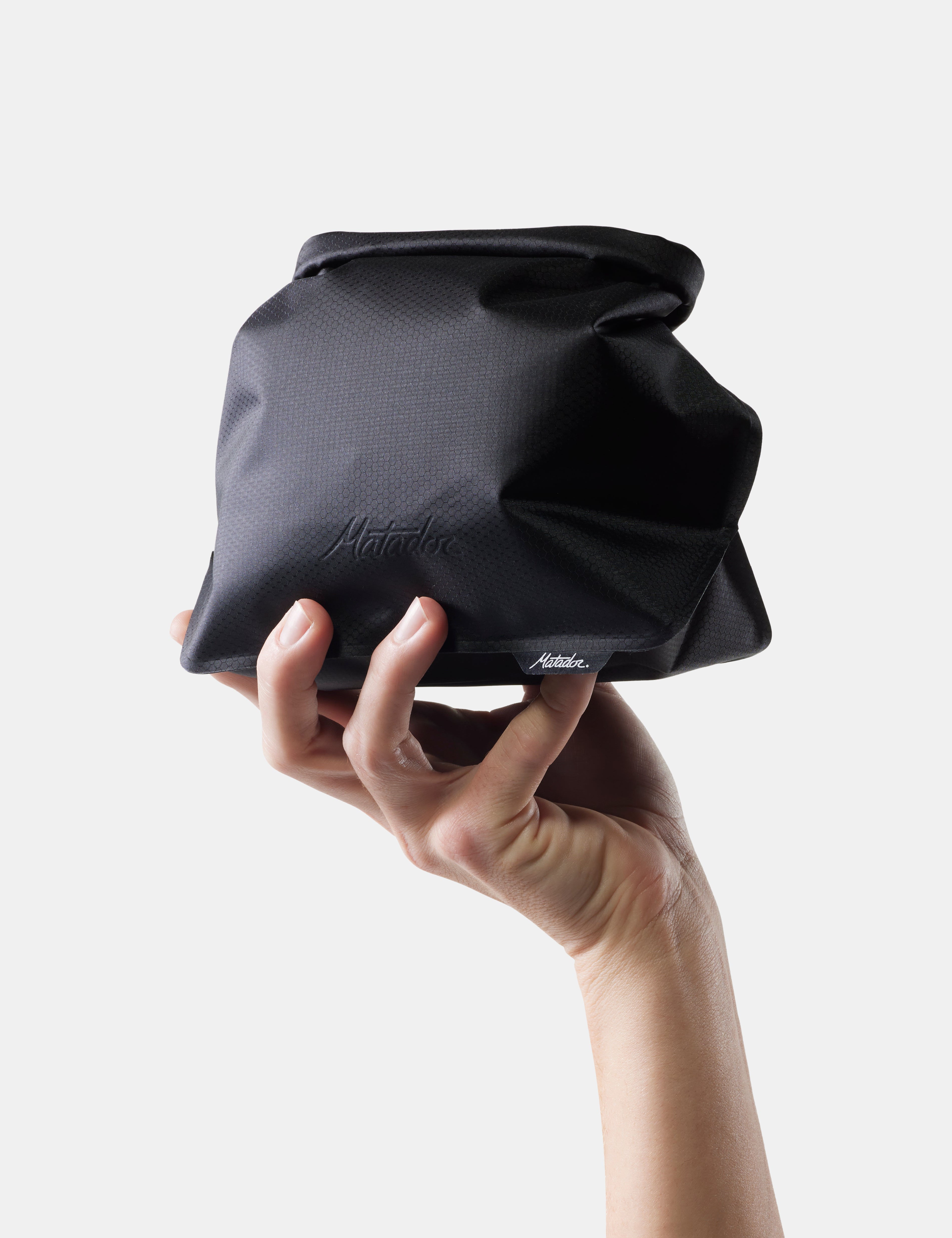 Hand holding a black fabric bag against a white background