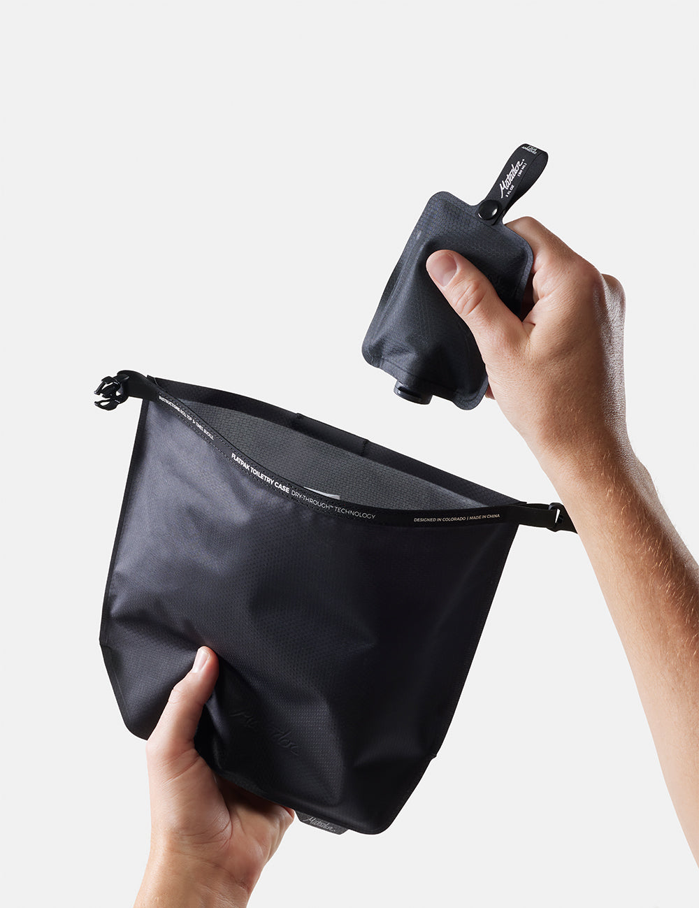 Person holding a black pouch with a smaller black item inside against a light gray background