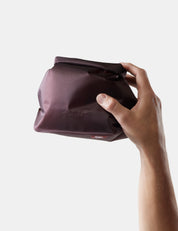 Hand holding garnet toiletry case on a light gray background