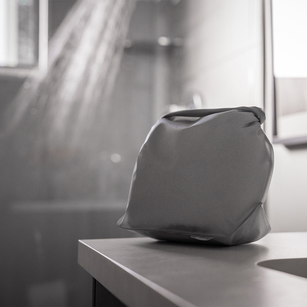 White toiletry case on bathroom counter with shower running in background