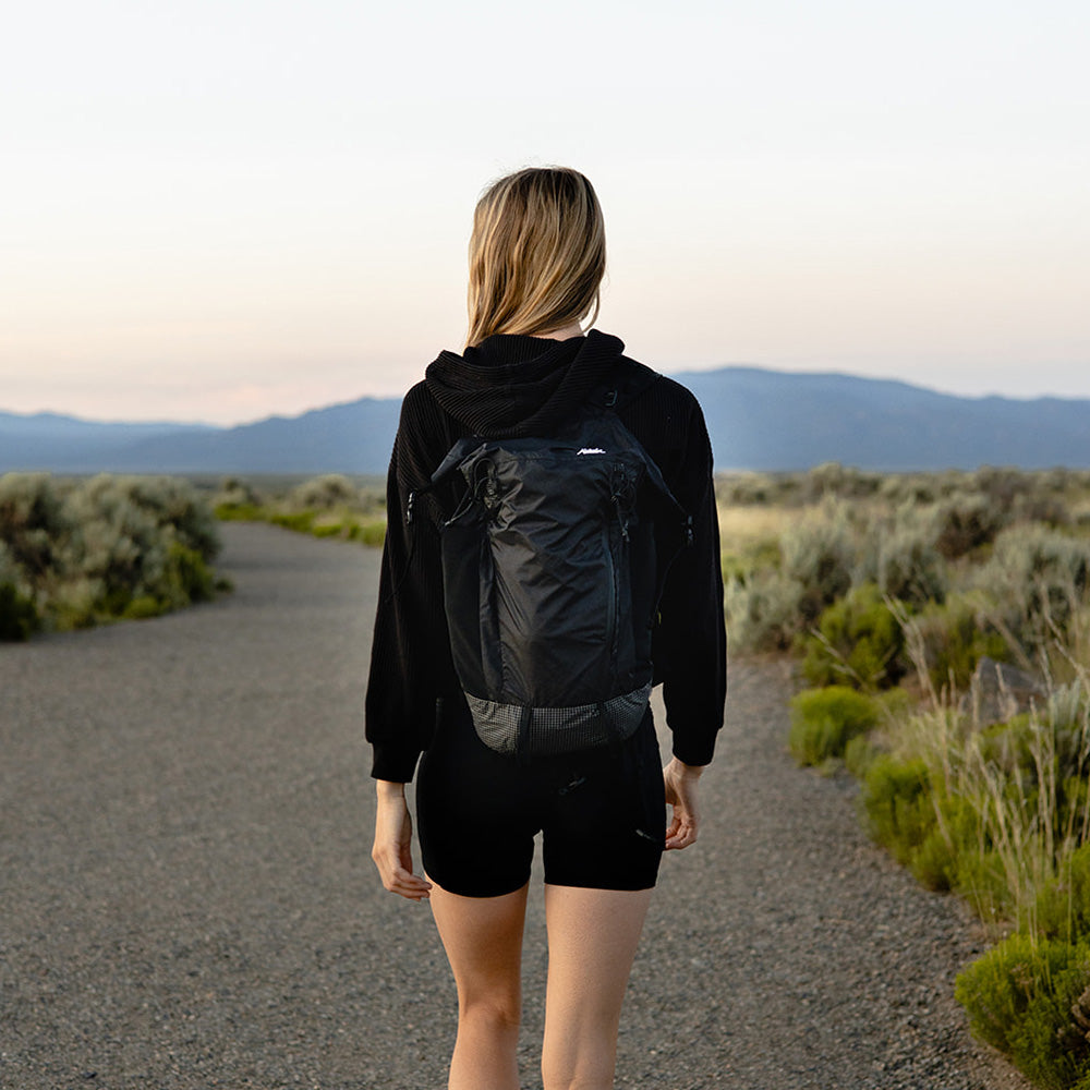 woman wearing black backpack, walking on desert path