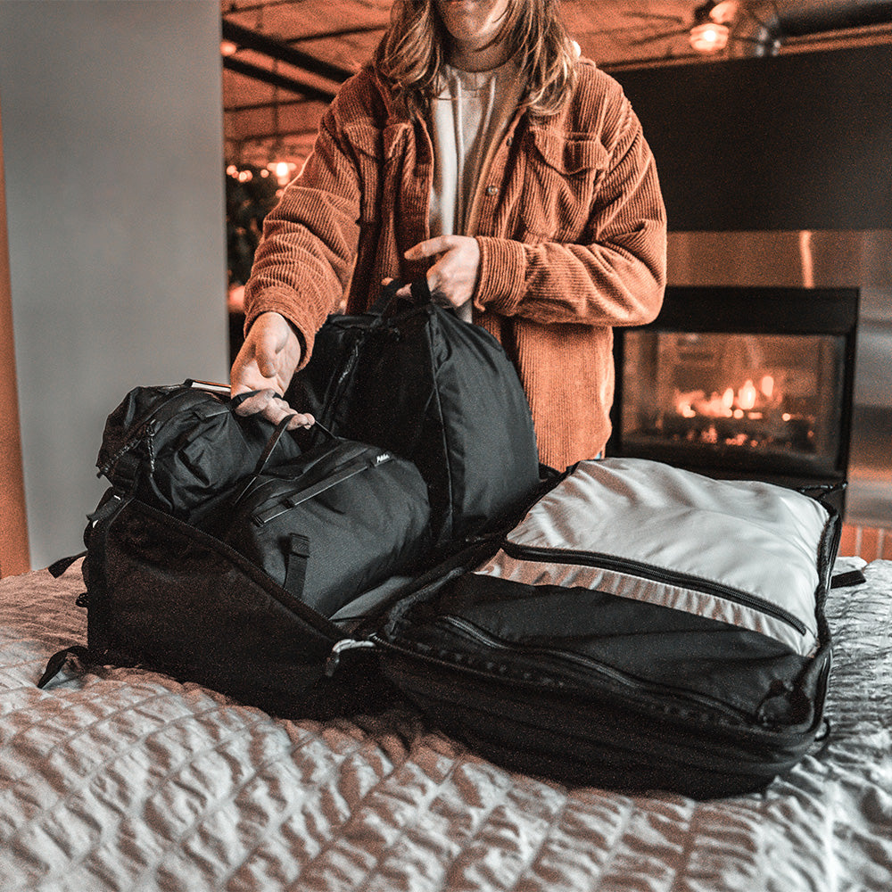 woman in cozy room, packing black gear cubes into travel pack