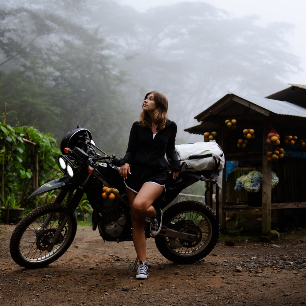 Woman on motorcycle in jungle with a white backpack