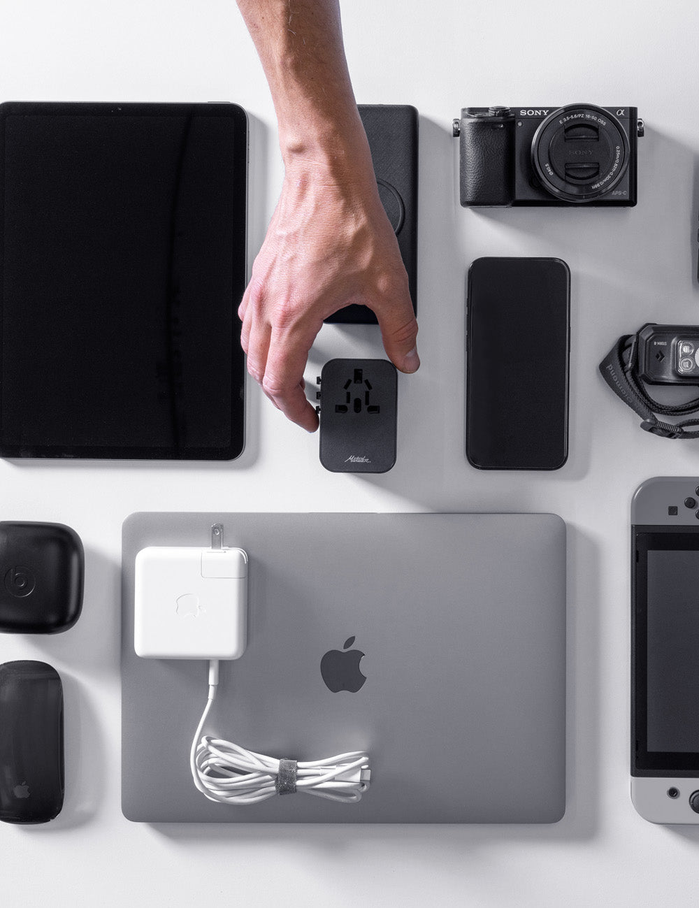 various electronics placed on white background with hand placing black travel adapter