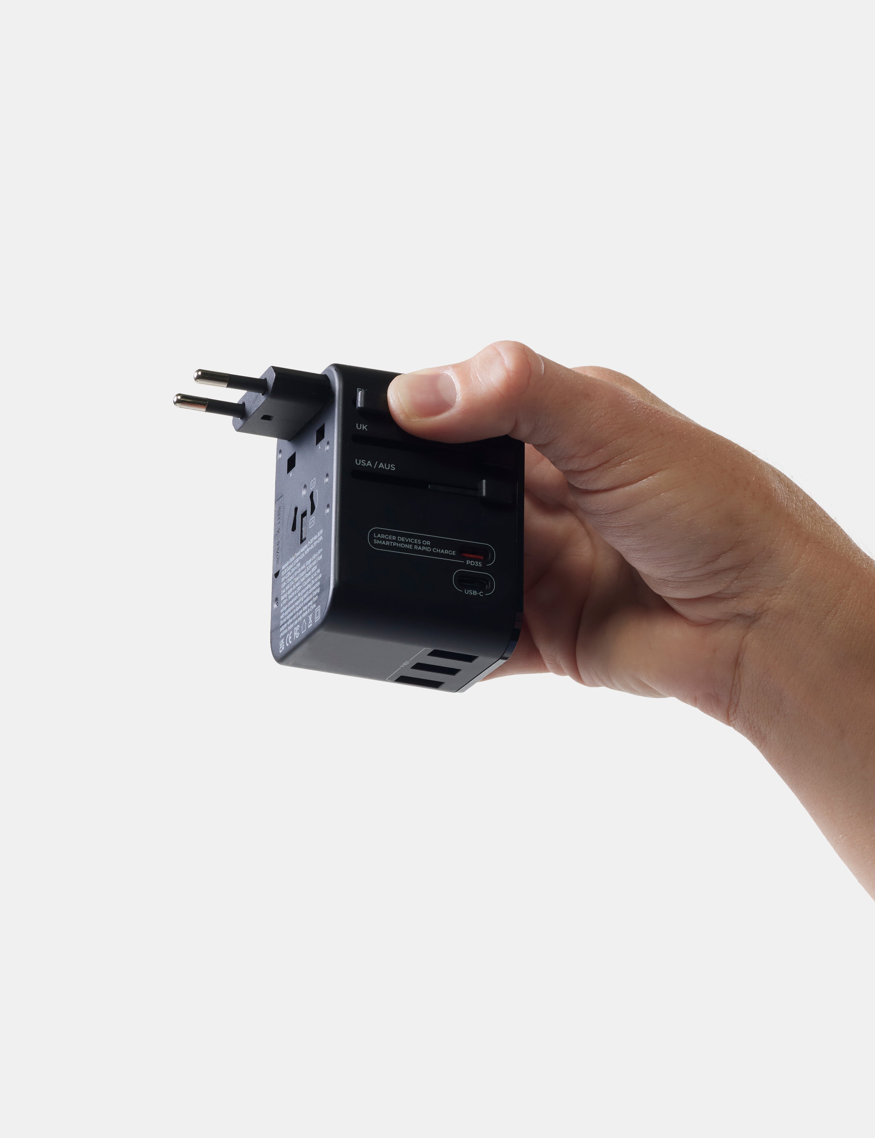 Hand holding a black travel adapter against a white background