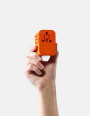 Hand holding an orange travel adapter against a white background