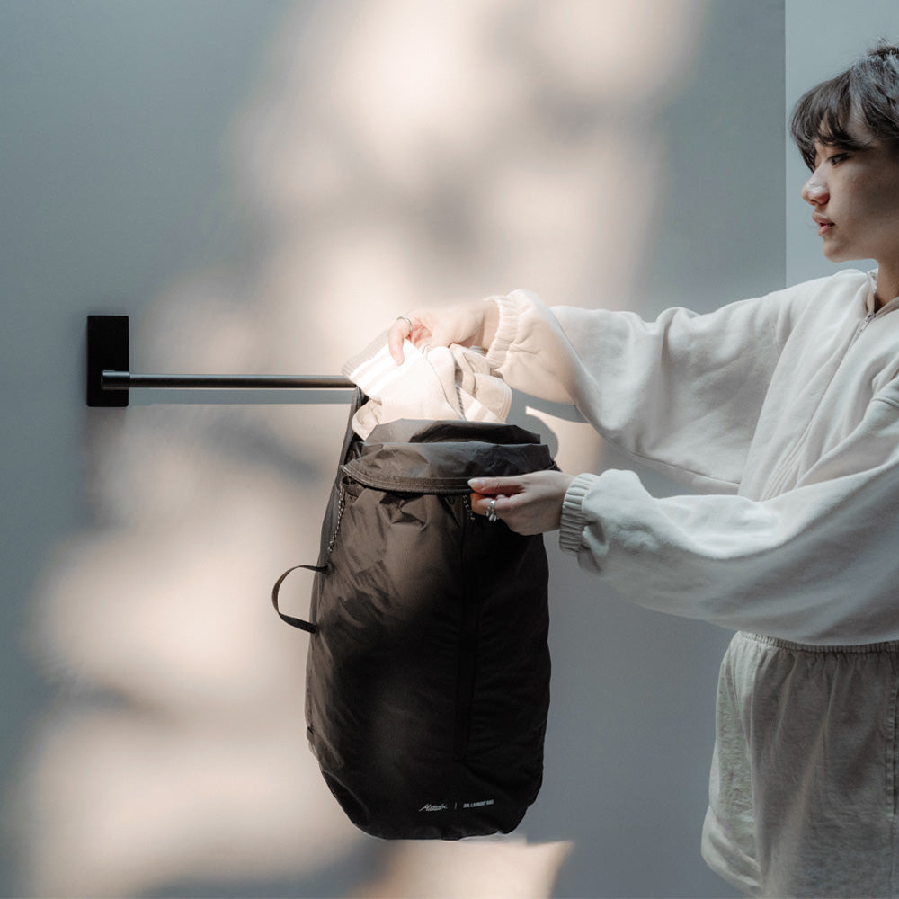 Woman placing dirty clothing into laundry bag hanging from towel rod