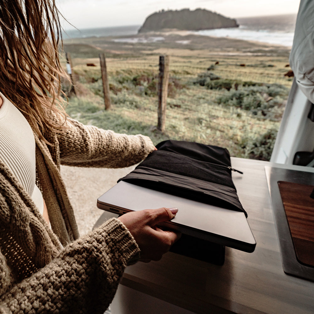 woman in travel van, pulling laptop out of base layer
