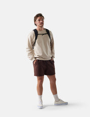 Man wearing a beige sweatshirt, brown shorts, and white sneakers on a white background