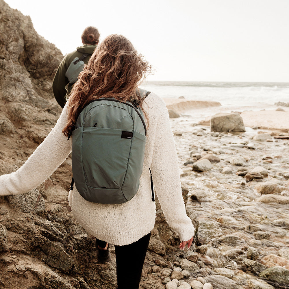 women walking on rocky shoreline wearing blue sling and backpacks