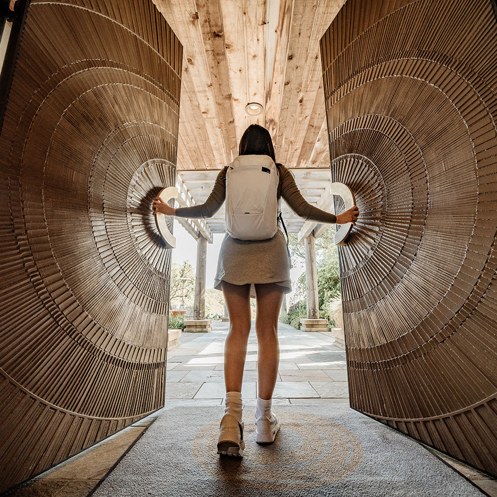 woman pushing open intricate wooden double doors, wearing white backpack