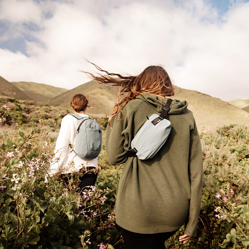 women in lush flowery field, wearing backpack and sling