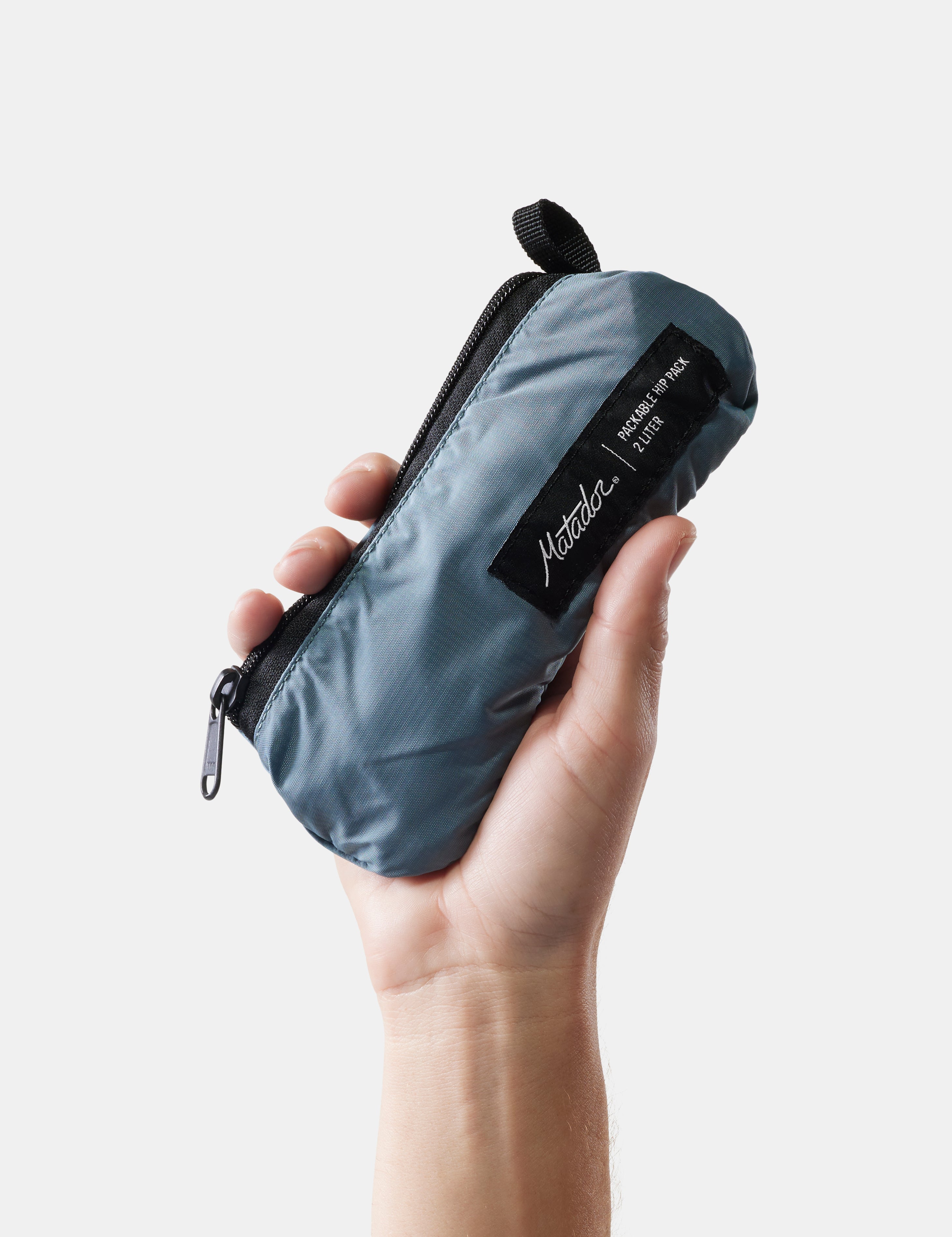 Hand holding a blue compact pack with a brand label on a light background