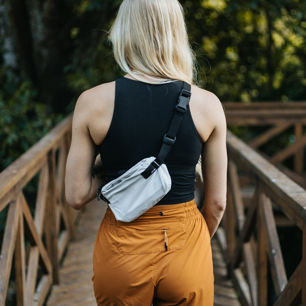 woman in bright orange pants, wearing white sling while walking on tropical boardwalk
