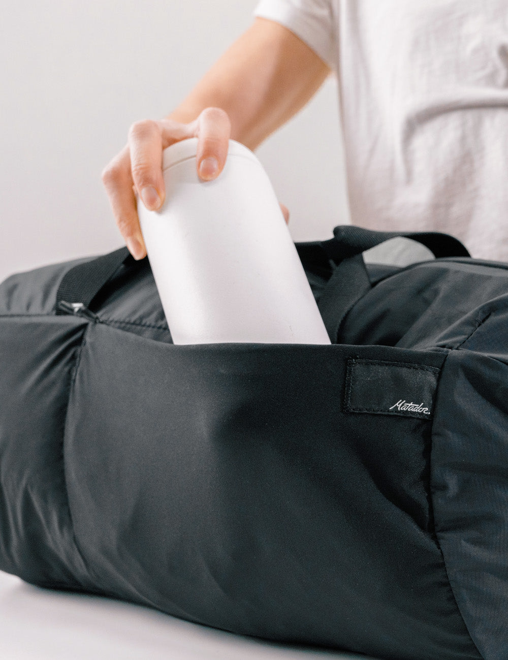 hand putting white water bottle into expandable side pocket of black duffle
