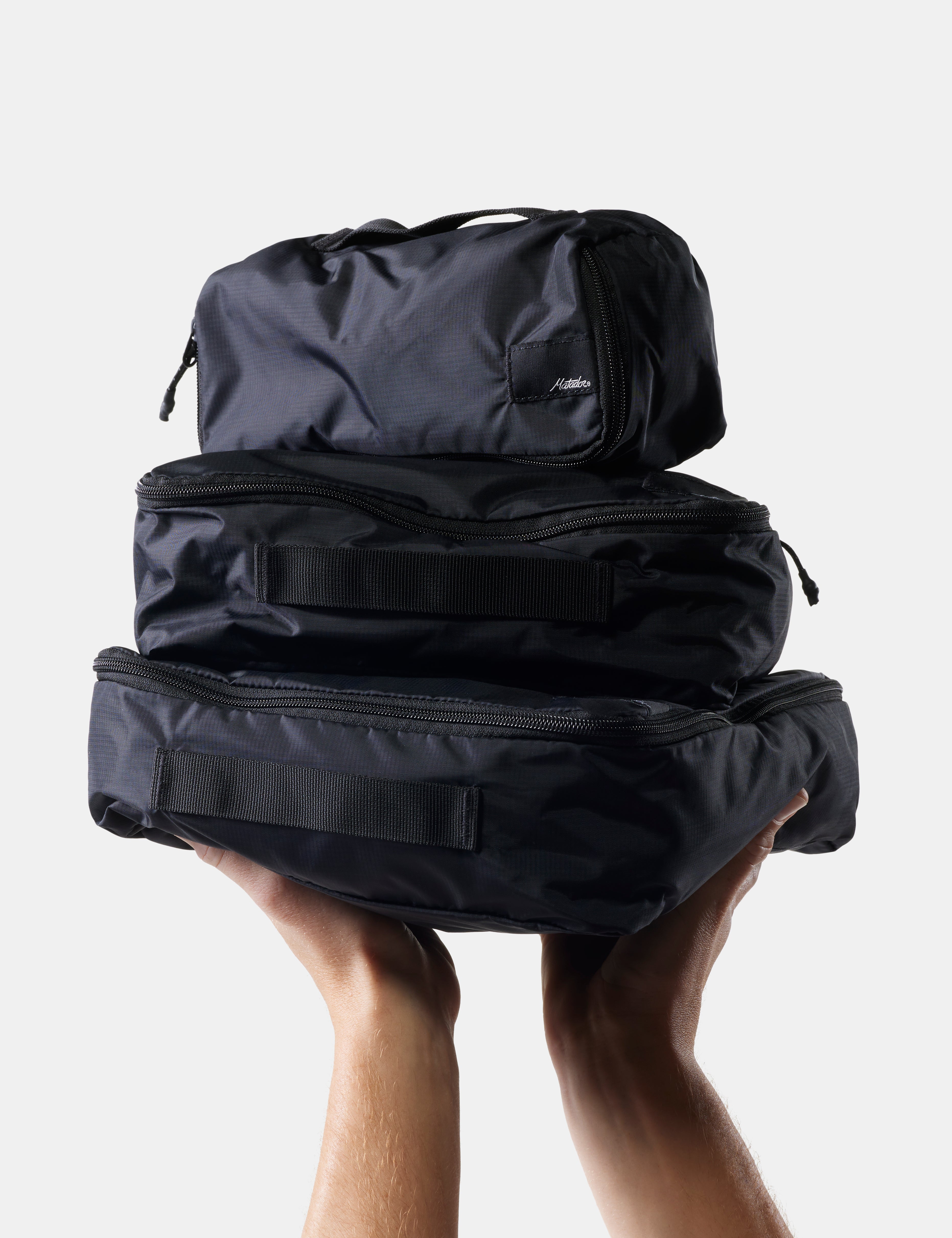 Stack of black travel bags held by a person against a light background