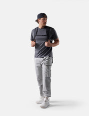 Man wearing a gray t-shirt, light gray cargo pants, white sneakers, and a black cap on a white background