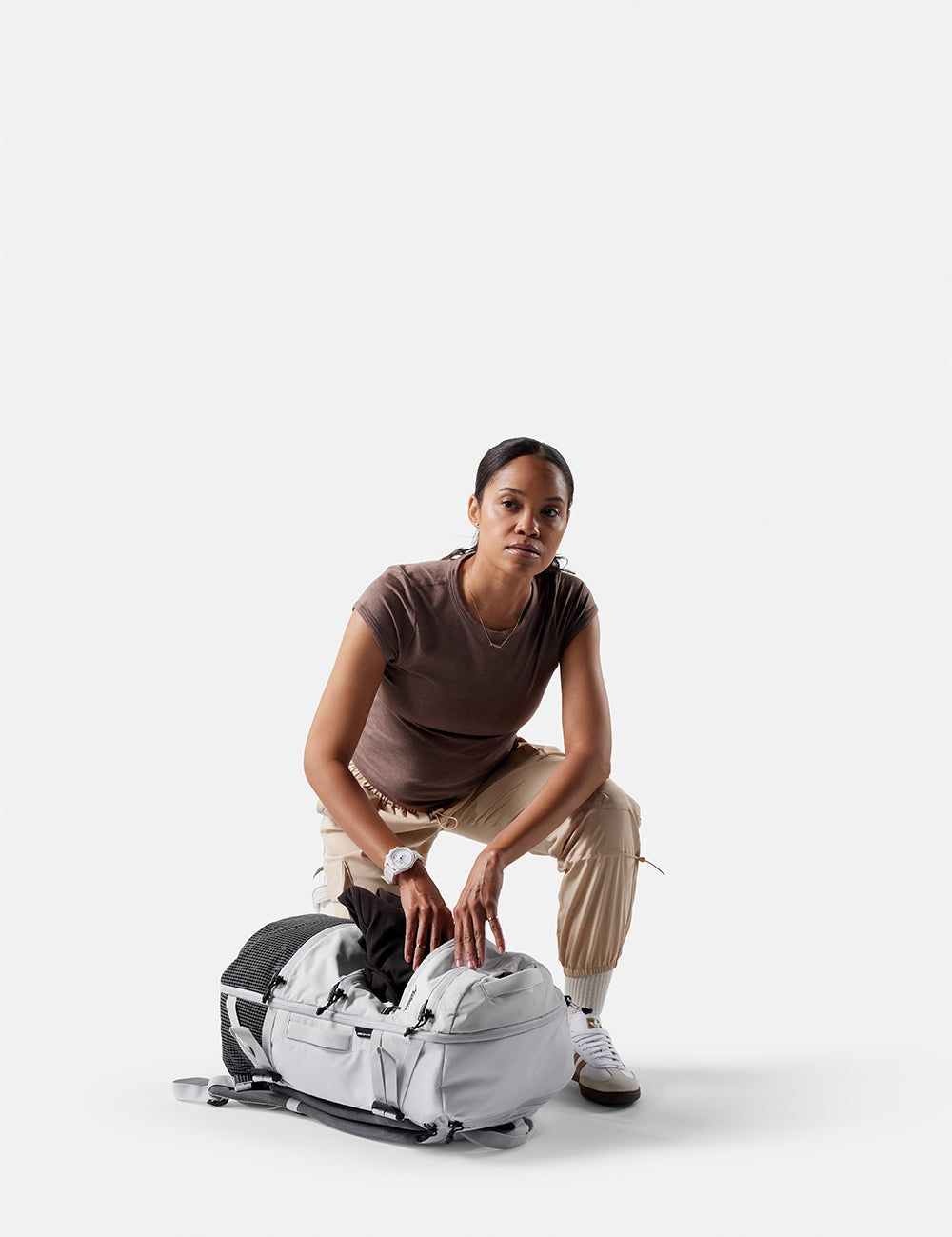 Woman organizing items in a large gray duffel bag on a white background