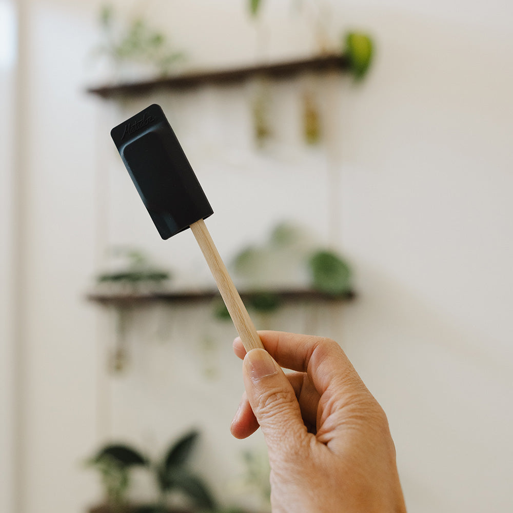 hand holding up toothbrush with black cap in plant-filled bathroom