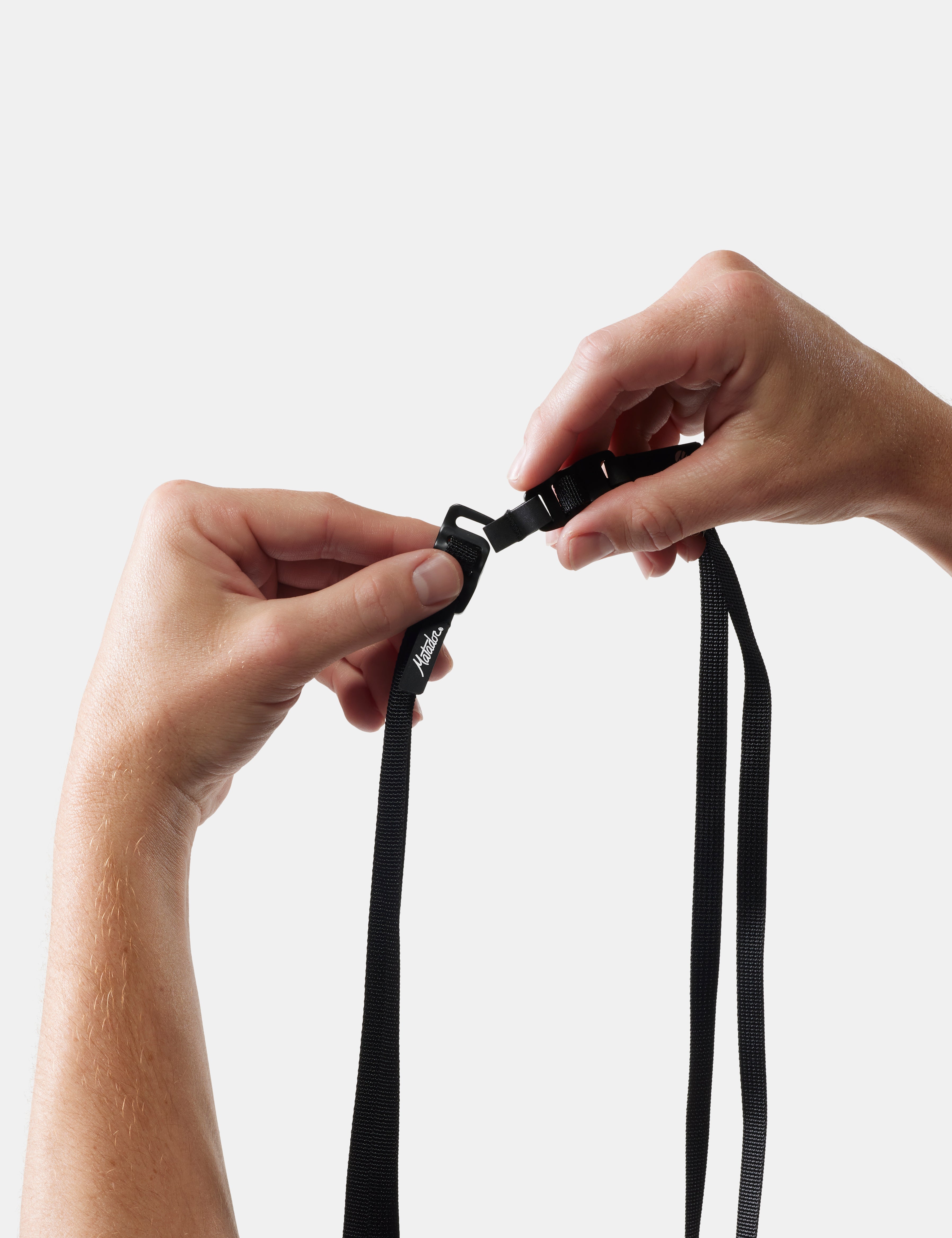 Close-up of hands tying a black lanyard against a white background