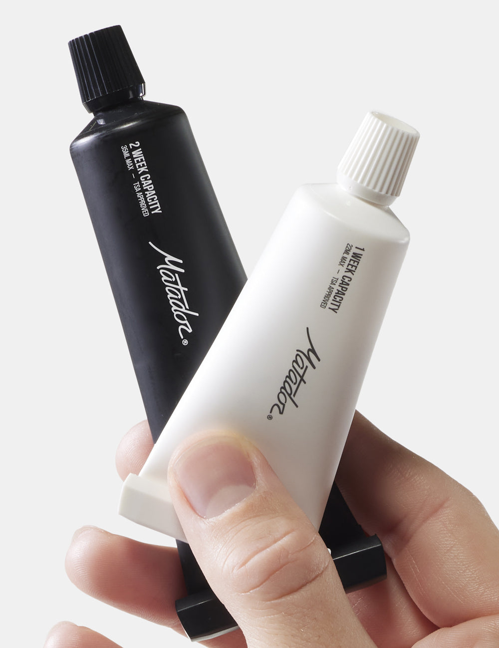 hand holding black and white toothpaste tubes—1 and 2 week capacity