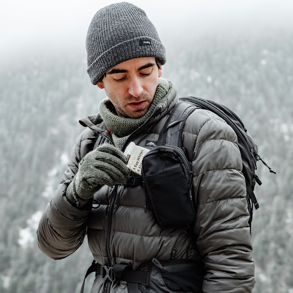 man in wintery wilderness pulling snack out of black speed stash