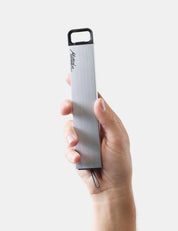 Hand holding a silver pill canister with a black top on a white background