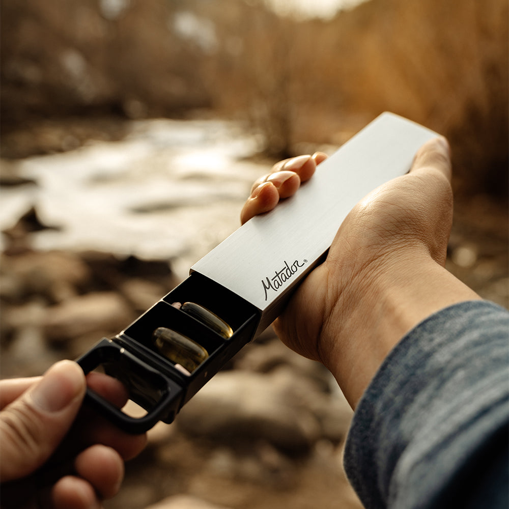 hands opening pill canister in front of sunset creek